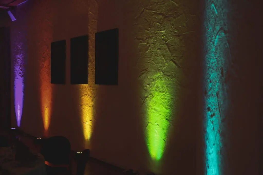 Uplights strahlen eine Wand in Orange, Grün und Türkis an